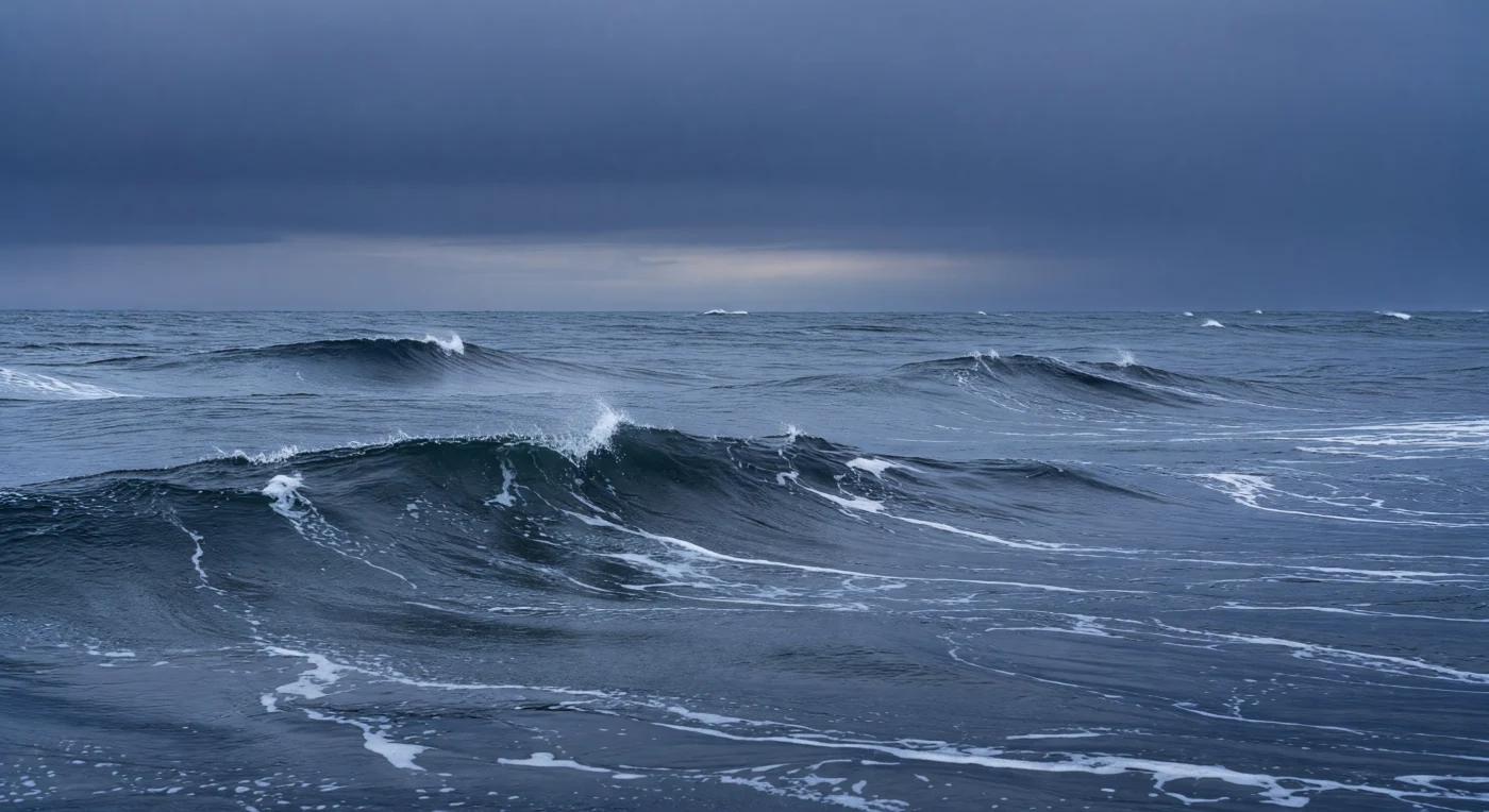 At the very threshold where atmosphere and ocean become indistinguishable, the sea surface under storm-force winds is one of the most energetically violent environments on the planet, a place where momentum, heat, and mass transfer between two fluids at rates that shape climate itself. Long swell trains generated by distant pressure systems propagate beneath shorter, steeper wind waves, their superimposition producing the characteristic cross-hatched chaos of open ocean gale conditions, while breaking crests inject billions of microscopic bubbles into the upper meter, briefly supersaturating the water with oxygen and generating the sea-salt aerosols that seed clouds far inland. The sea-surface microlayer — that biochemically extraordinary film spanning barely a millimeter — is perpetually destroyed and reformed here, its concentrated organic molecules, bacteria, and lipids shredded by each breaking wave and redistributed as spindrift racing low across the water in pale, fast-moving veils. Langmuir circulation organizes the subsurface turbulence into paired helical cells aligned with the wind, collecting foam and biological material into the long windrows visible as combed streaks across the troughs, while the mixed layer deepens with every hour of sustained gale, entraining cooler, denser water from below and erasing the seasonal thermocline. This is the ocean at its most exposed and most consequential — a raw coupling of sky and sea that has operated without interruption across billions of years, indifferent and immense.